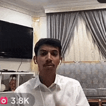 a man wearing ear buds is sitting in front of a television with 3.8k written in the corner
