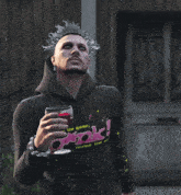 a man in a black hoodie holds a glass of wine in front of a wooden building
