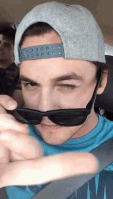 a young man wearing sunglasses and a hat looks at the camera