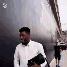 a man in a white shirt is smiling while holding a black purse