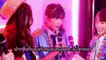 a group of girls are standing in front of microphones in a room with purple lighting .