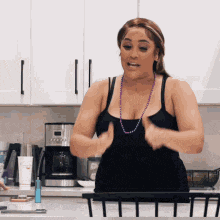 a woman in a black tank top is standing in a kitchen holding her breasts .