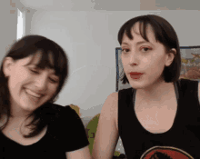 a woman wearing a black tank top with a dinosaur on it is smiling next to another woman