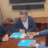a group of men are sitting at a table with papers and a cup of coffee .