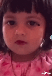 a little girl is wearing a pink dress and a necklace .