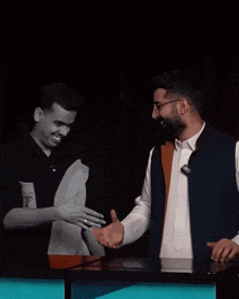 two men are shaking hands in a dark room and one has a sticker on his shirt that says ' x '