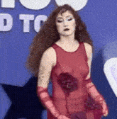 a woman wearing a red dress and red gloves is standing in front of a blue background .