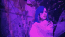 a woman with blue hair and a white shirt is standing in front of a purple background .