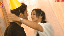 a man wearing a party hat is being kissed by a woman wearing a white shirt