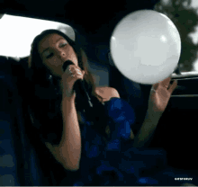 a woman in a blue dress is singing into a microphone in a car while holding a balloon .