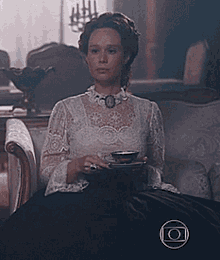 a woman in a white lace top sits on a couch holding a cup of tea