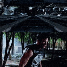 a man wearing a punisher shirt stands in front of a railroad track