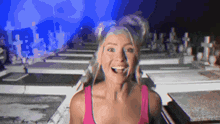 a woman in a pink tank top stands in a cemetery