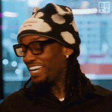 a man wearing glasses and a beanie is smiling with the be tv logo in the background