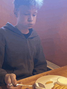a young boy sits at a table with a plate of food