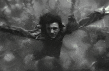 a black and white photo of a man swimming in the water with his arms outstretched .