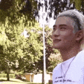 a young man wearing a headband and a necklace is standing in a park with trees in the background .