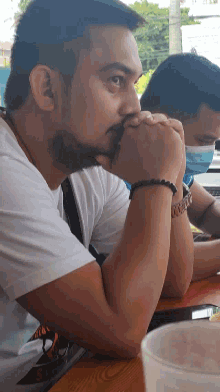 a man with a beard is sitting at a table with another man wearing a face mask