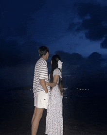 a man and a woman standing on a beach looking at the ocean
