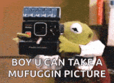 kermit the frog is holding a polaroid camera over his head and says `` boy u can take a mufuggin picture '' .