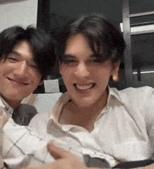 two young men are sitting next to each other and smiling for the camera .