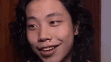 a close up of a young man with long curly hair smiling .