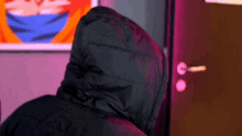 a person wearing a black jacket with a hood is standing next to a door .