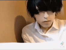 a young man with black hair and a white shirt is sitting in a chair .