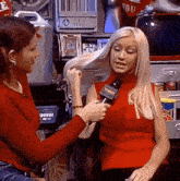a woman in a red shirt is talking into a microphone while another woman holds her hair