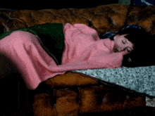 a person wrapped in a pink blanket sleeping on a brown leather couch