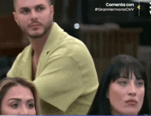 a man in a yellow shirt is sitting in front of two women and a sign that says commenta con #granhermanochv