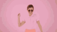 the woman is wearing sunglasses and a pink shirt and is dancing on a pink background .