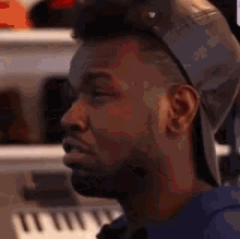 a man wearing a hat and a blue shirt is sitting in front of a piano keyboard .