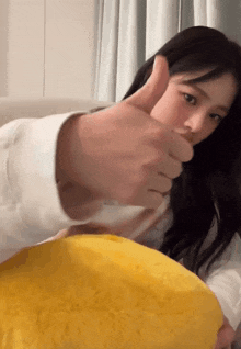 a woman is giving a thumbs up sign while holding a yellow pillow .