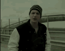 a man wearing a beanie and a varsity jacket is standing on a highway .