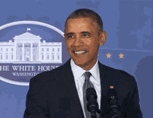a man in a suit and tie stands in front of microphones in front of the white house