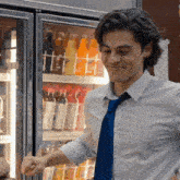 a man in a blue tie is standing in front of a fridge full of soda