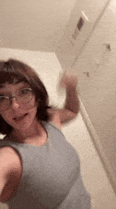 a woman wearing glasses and a grey tank top is taking a selfie .