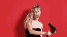 a woman is holding a hair dryer in her hand and blow drying her hair against a red background .