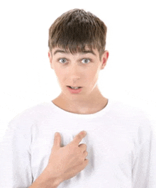 a young man in a white shirt is pointing to his chest .