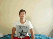 a young man is sitting on a bed wearing a t-shirt that says jones