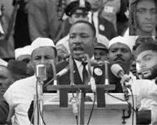 a man is giving a speech in front of a crowd of people .