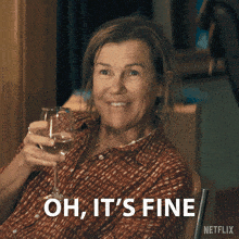 a woman holding a glass of wine with the words " oh it 's fine " behind her