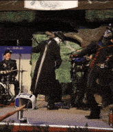 a man in a black coat is playing a guitar in front of a sign that says " skye "