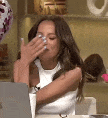 a woman covering her face with her hand while sitting in front of a laptop