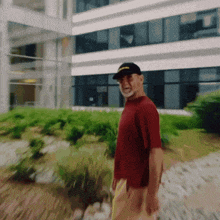 a man wearing a red shirt and a black hat is walking in front of a building