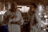 two men are standing in a kitchen talking to each other