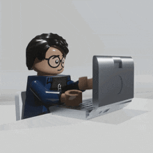 a lego figure is typing on a laptop with a smiley face on the screen