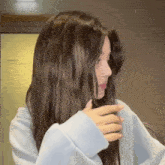 a woman with long brown hair is wearing a light blue sweater and covering her face with her hand .