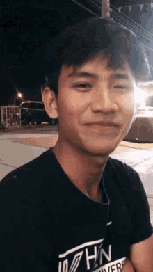 a young man wearing a black shirt with the word hn on it smiles at the camera .